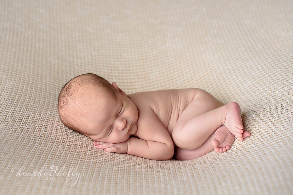 newborn boy snuggled on tan blanket