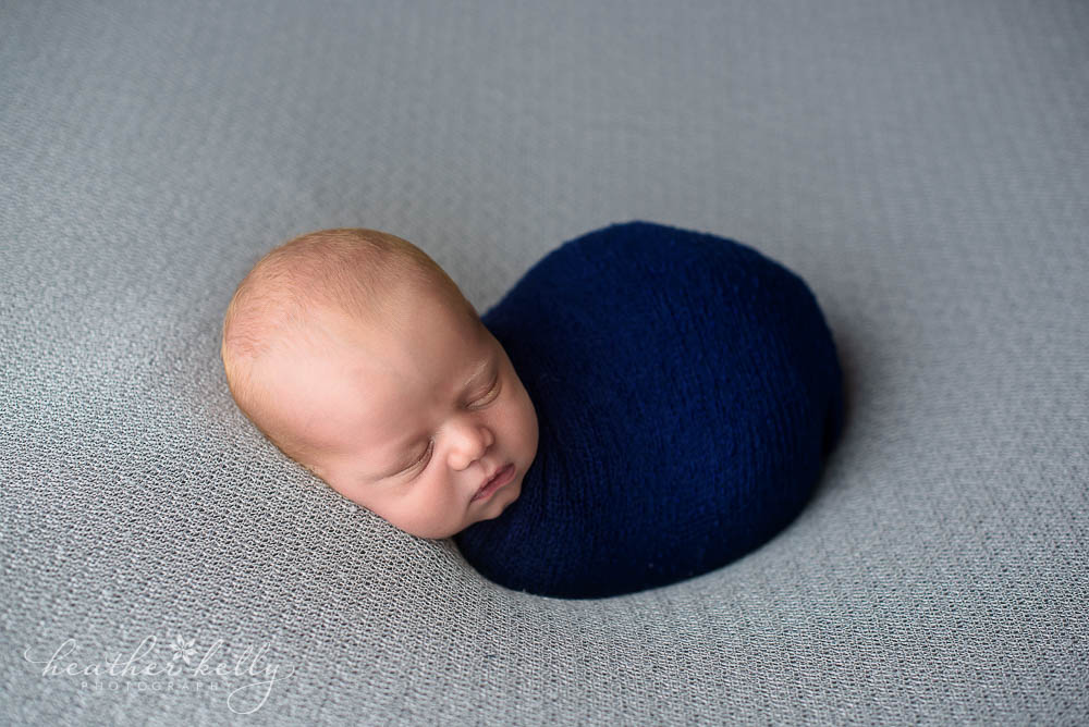 newborn baby wrapped up snug. Navy  wrap on gray backdrop