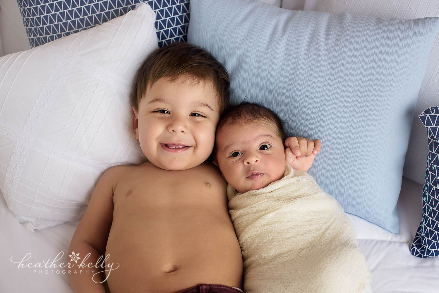newborn photography photo of toddler brother holding new baby brother on bed