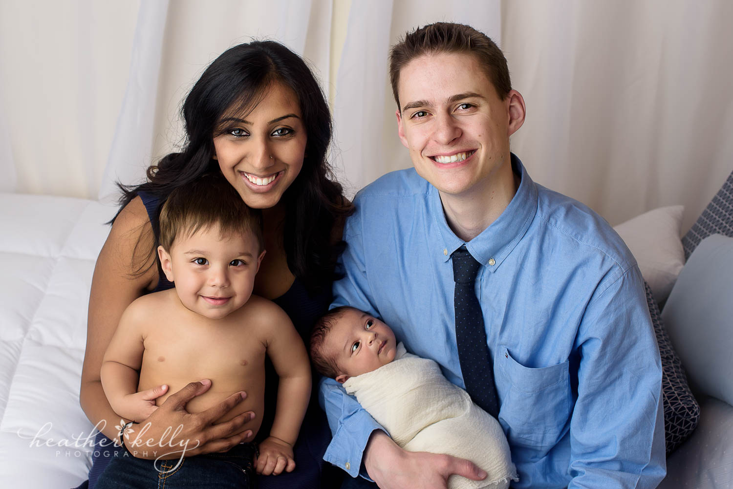newborn family photography photo. Family of 4 on bed with toddler brother and newborn baby. 
