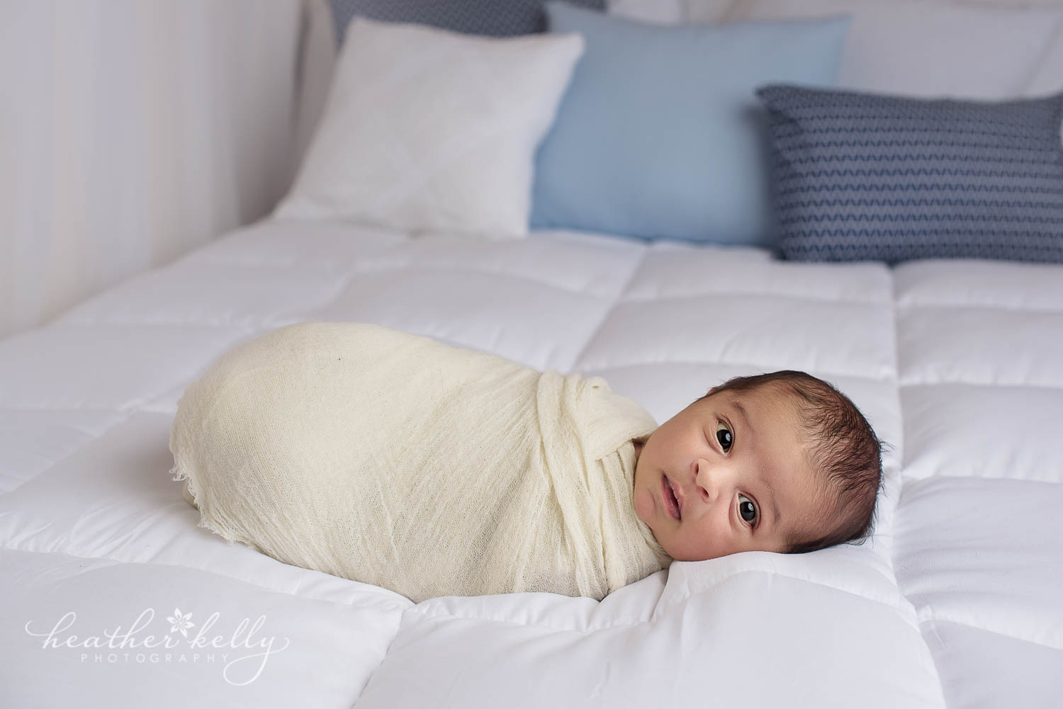 newborn boy wrapped in cream on white bed photo with blue pillows. Newborn photography. 