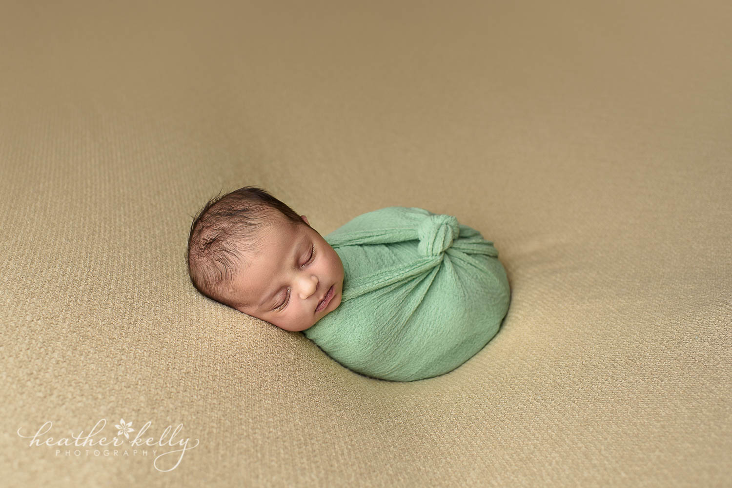 newborn photography. Baby boy in green wrap with knot on tan backdrop. 