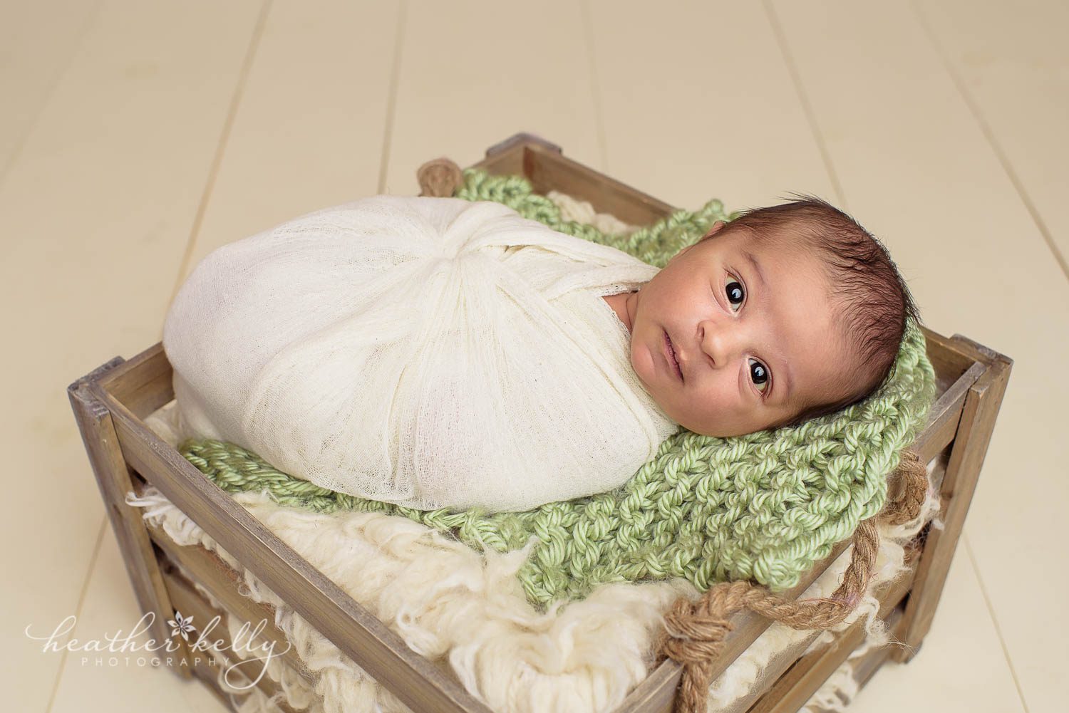 newborn photography. Awake newborn boy photo in cream wrap on top of crate. Cream wood floor. 