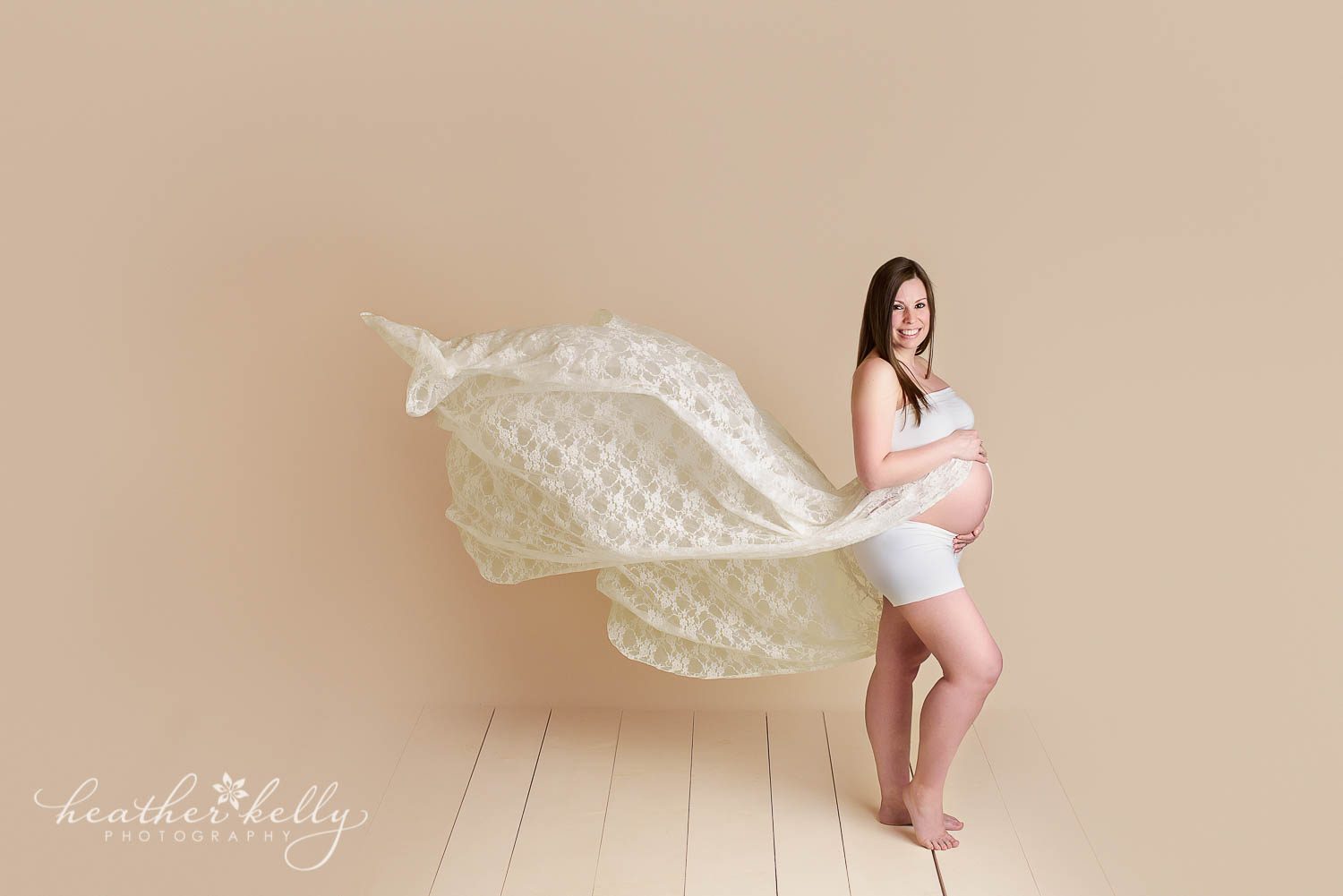 maternity photography. White lace gown flying in air in maternity portrait studio. 