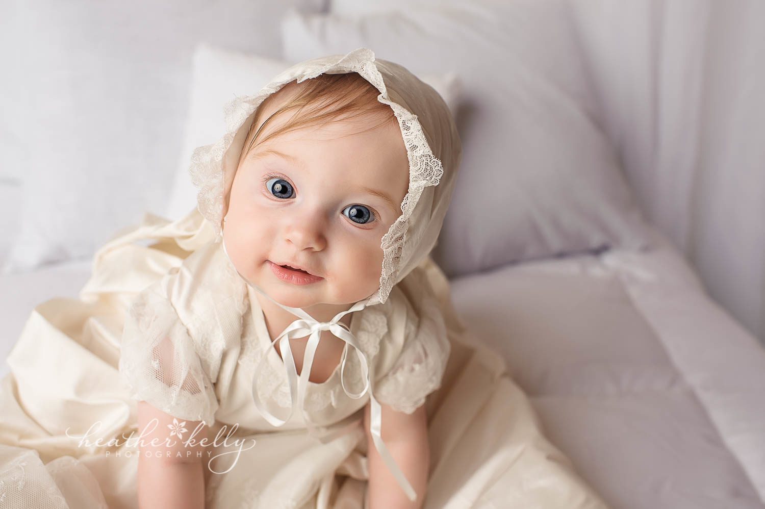 photo of baby girl sitting on bed in baptism gown photo. ct baby photographer Heather Kelly Photography. 