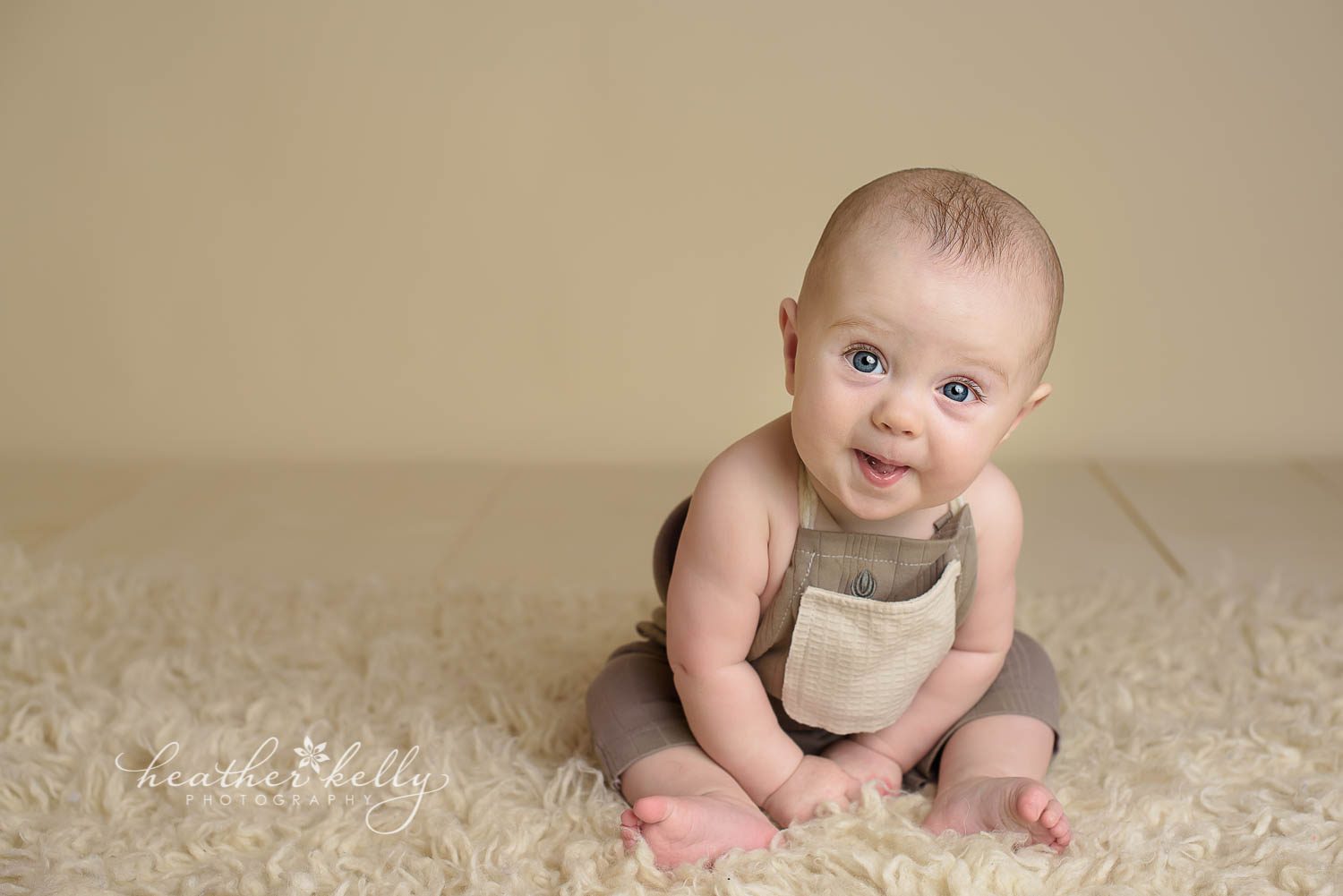7 month boy sitting during photo session. Cream wood floor and background. Wearing an adorable sitter outfit. newtown baby boy by ct photographer heather kelly photography.