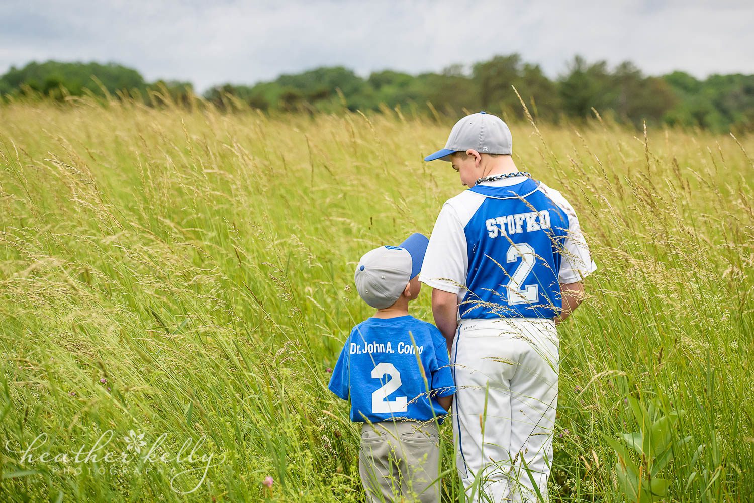 brothers in field facing away and looking at each other while wearing baseball uniforms. poughquag ny family photography