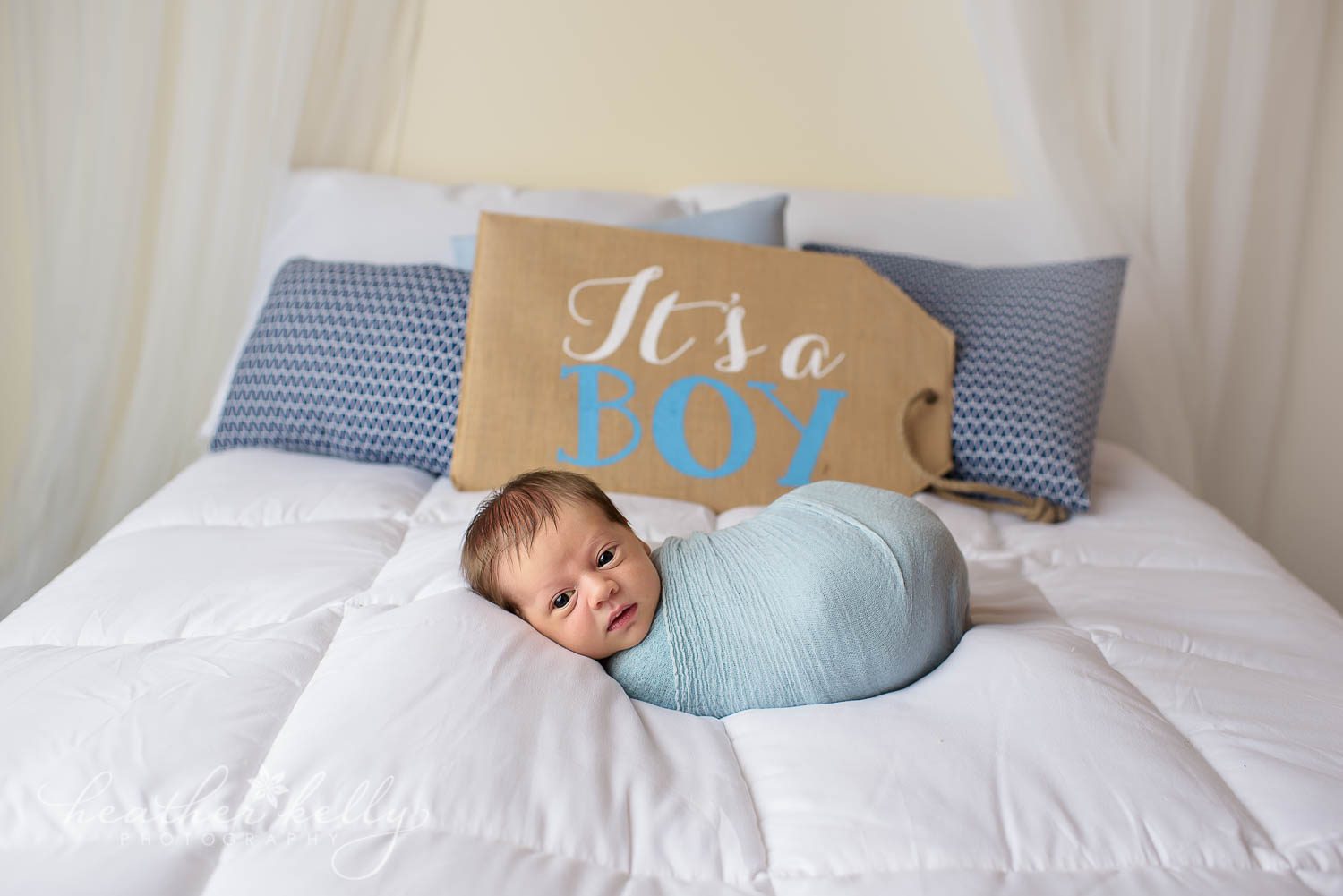 wrapped newborn boy on bed with it's a boy sign behind him