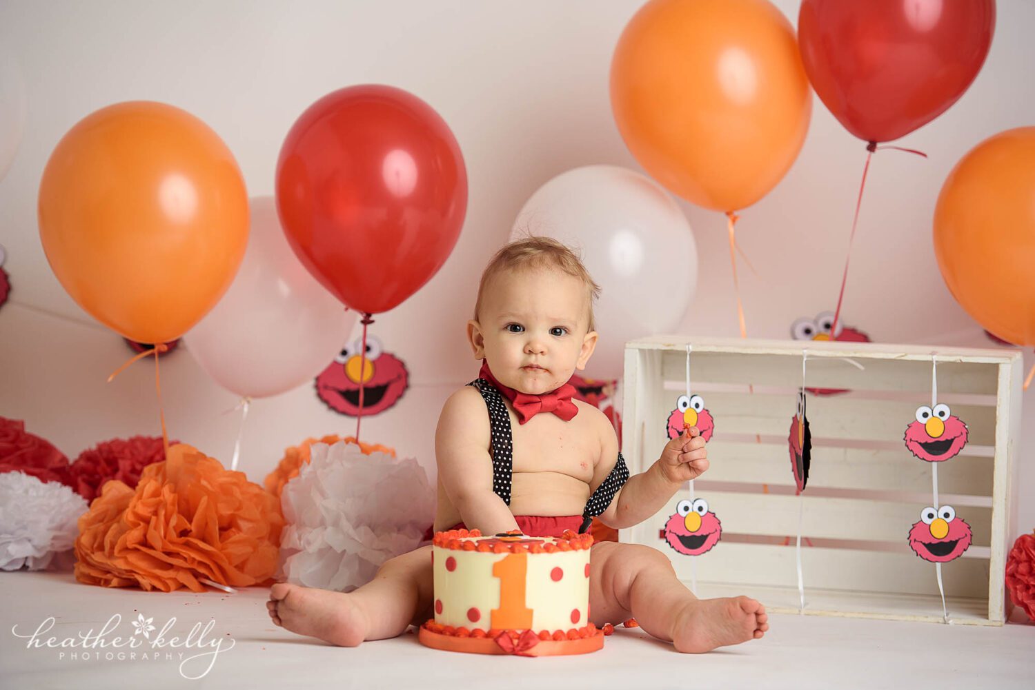picture of a one year old boy sticking his hand into an elmo decorated cake for his Stratford CT cake smash session by Heather Kelly Photography