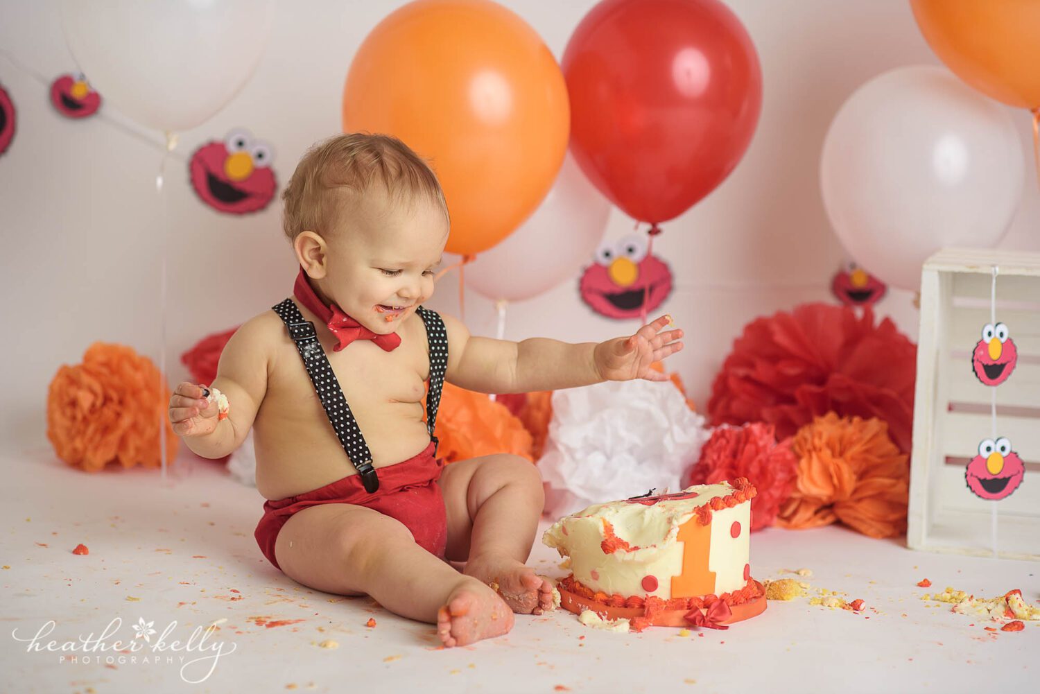 A one year old boy smiles and looks at his smashed in elmo cake during his Stratford CT Cake Smash photography session. 