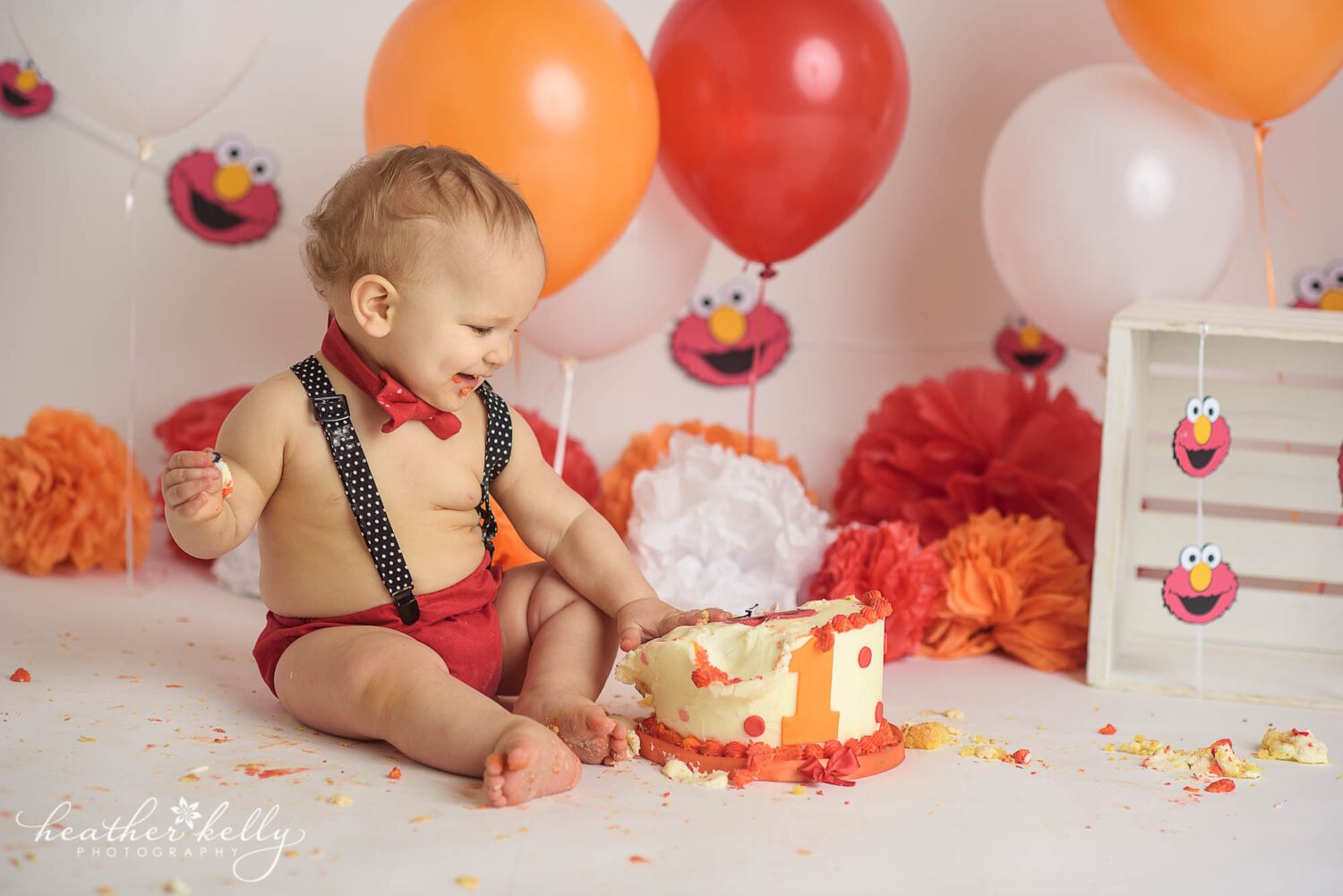 A one year old boy smiles and touches his smashed in elmo cake during his Stratford CT Cake Smash photography session. 