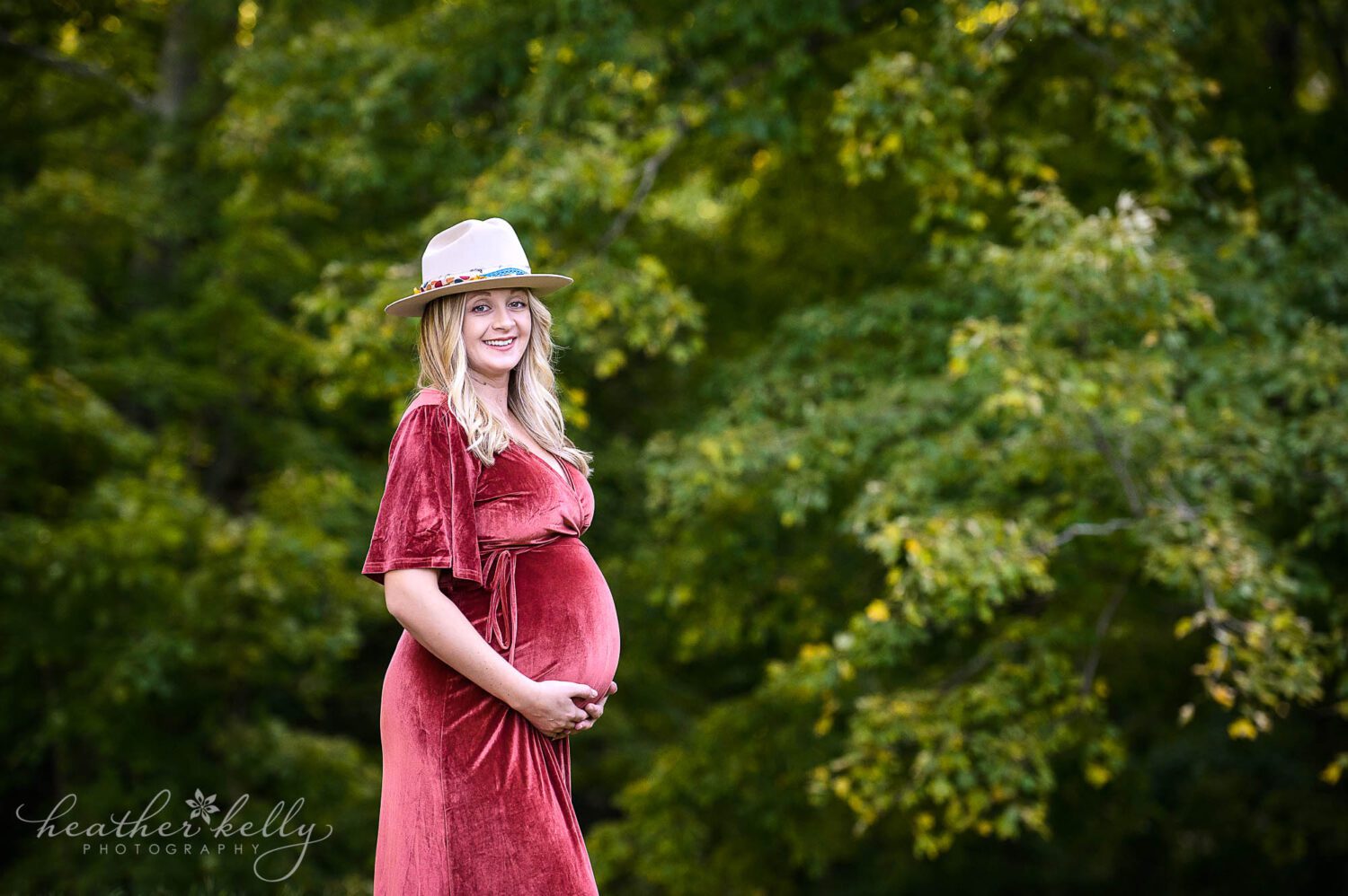 Bridgeport CT maternity photography. A maternity photography session with mom in a dress wearing a hat. She is smiling at the camera and her hands are under her belly. 