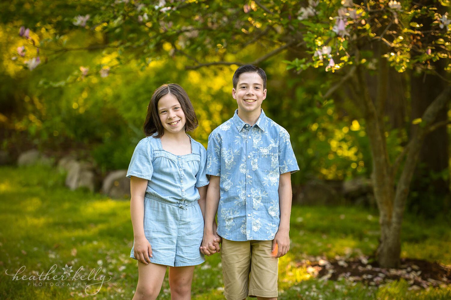 a brother and sister holding hands and looking and smiling at the camera. 
