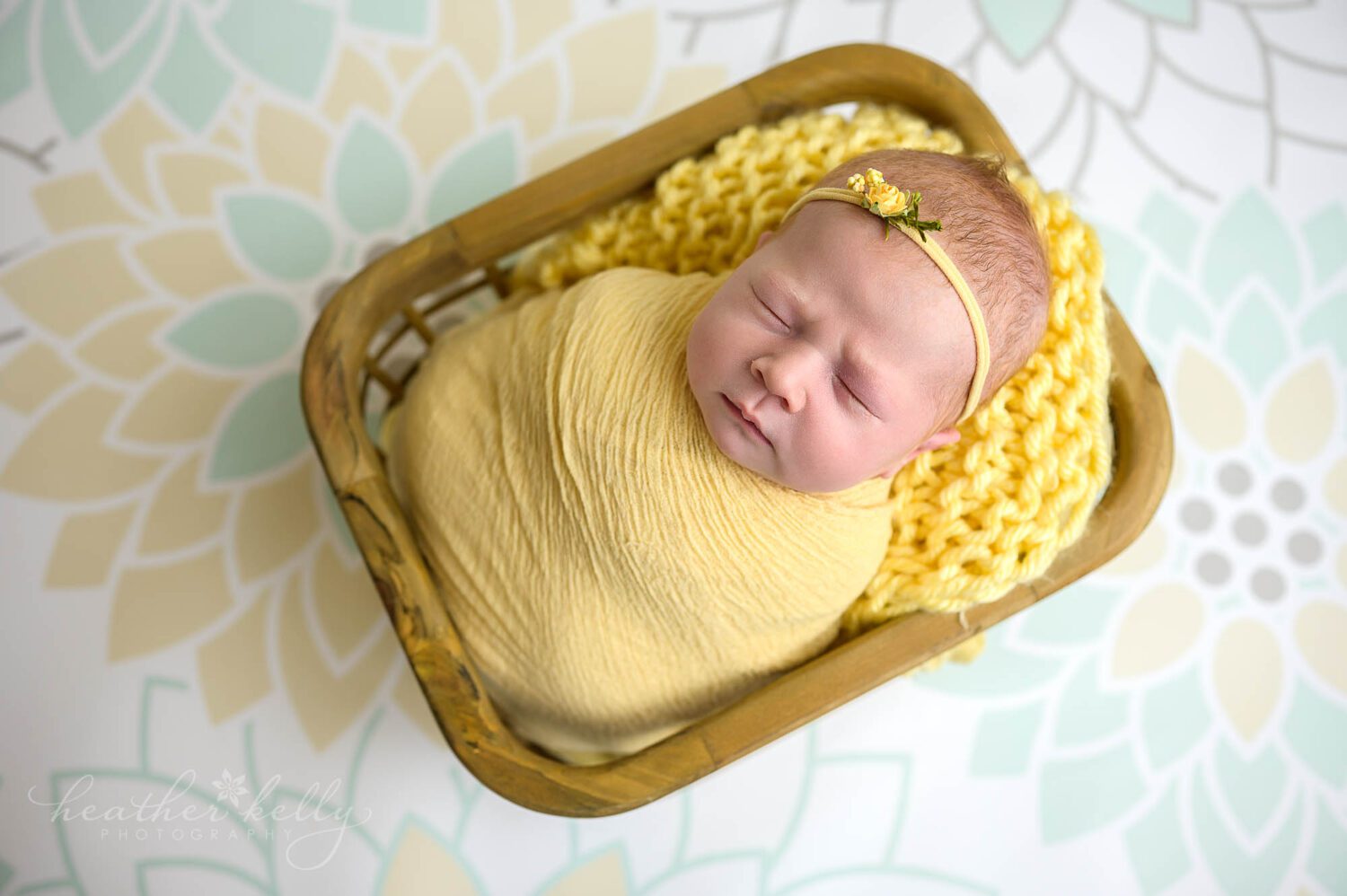 a baby girl is wrapped in yellow and posed in a crate. she is sleeping. 
