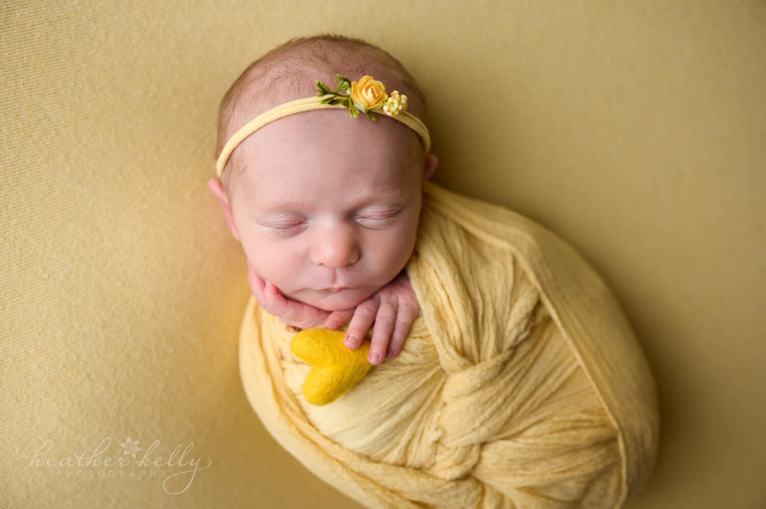 wrapped in yellow, and holding a small yellow felted heart. A sleeping newborn is posed on yellow. 