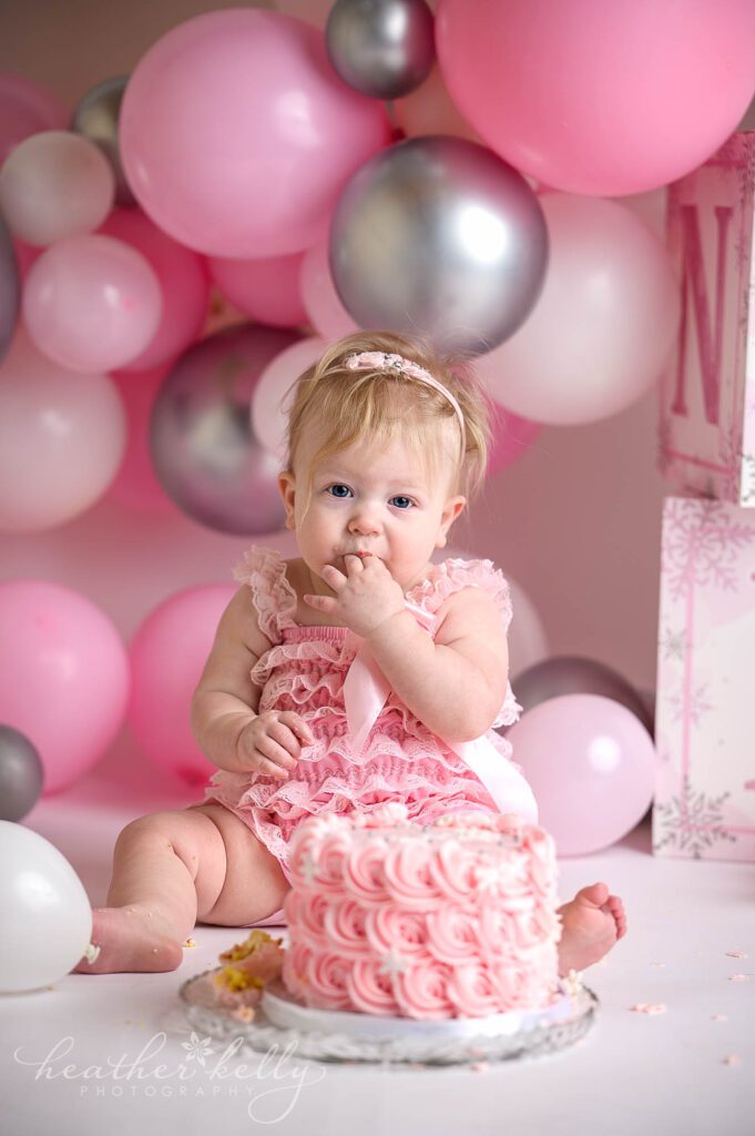 a one year old girl is eating a cake during her sandy hook ct cake smash photography session 