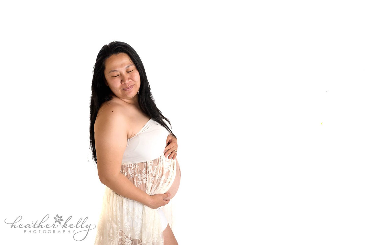 a mom to be wearing a white lace maternity gown during her maternity photography session. There is a high key white background. Danbury maternity photographer