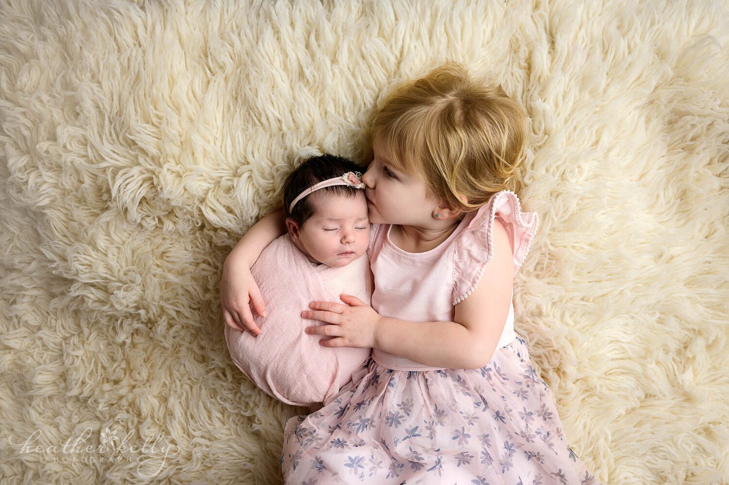 a girl kisses her newborn sister who is swaddled in pink. 