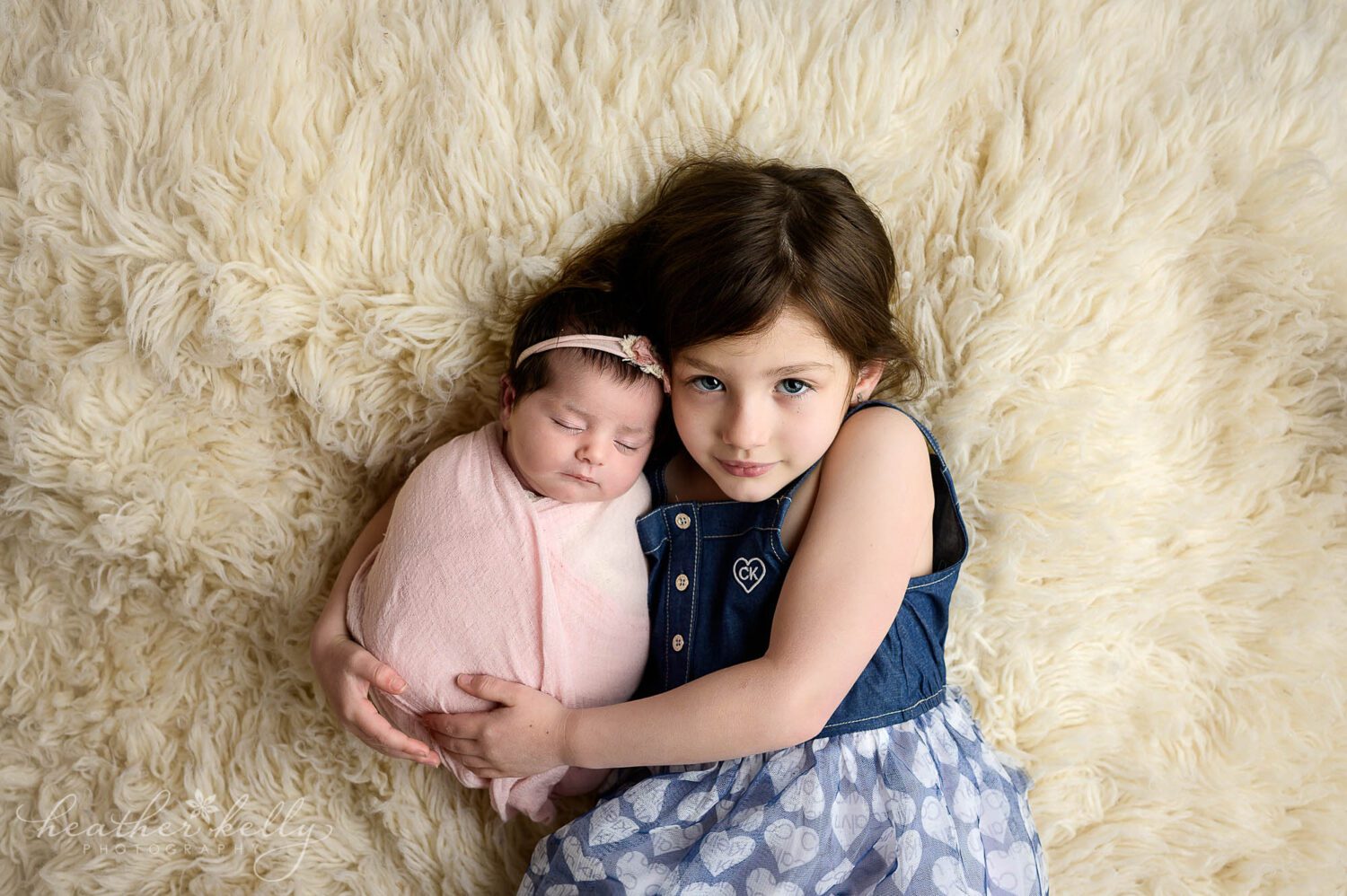 a girl cuddles with her newborn sister who is swaddled in pink 