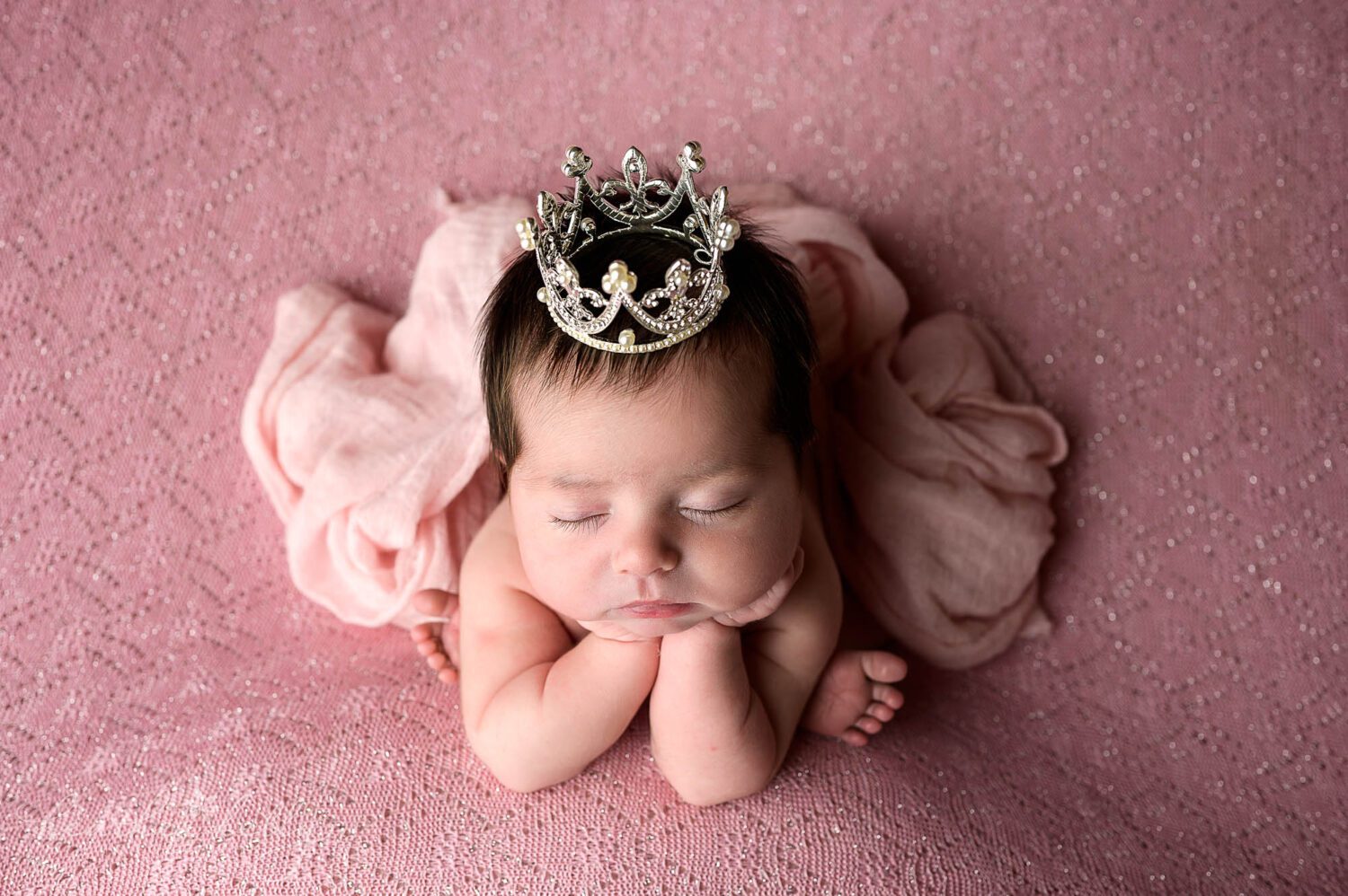 a newborn girl wears a crown and has a pink wrap draped over her. She is wearing a crown and in a froggy pose. 

newborn photos in newtown