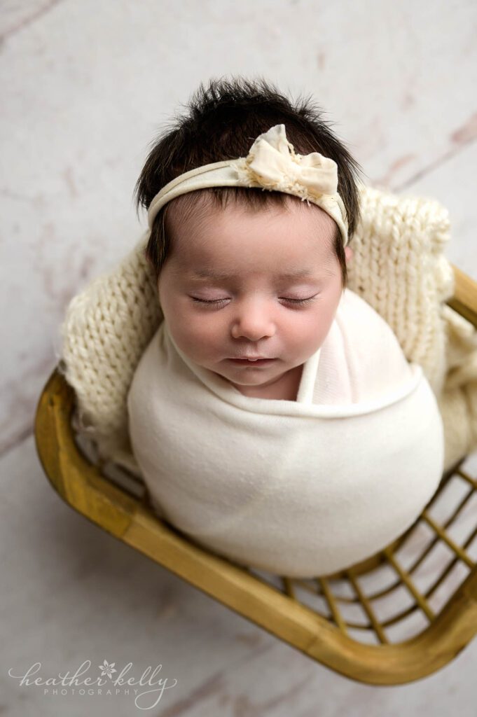 a newborn girl is sleeping and swaddled in white. She is in a wood crate. 

newborn photos in newtown