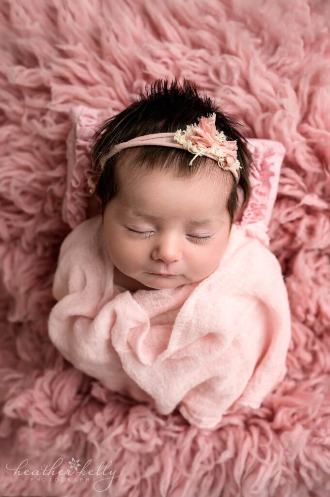 a newborn photography session. A newborn girl is wrapped in pink. 
