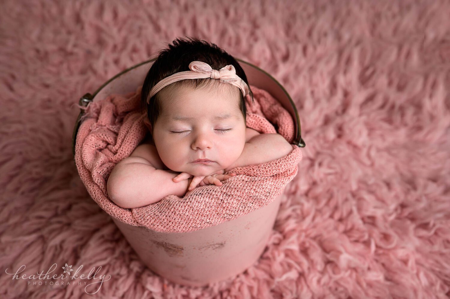 a newborn photo session of a baby girl sleeping in a pink bucket. 